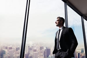 Empresário olhando pela janela do escritório - capital de giro para crescer: qual o momento certo de investir na sua empresa?